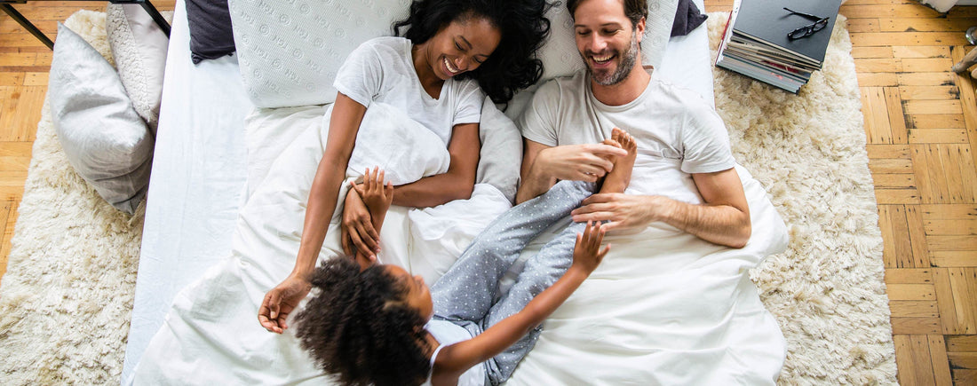An arial picture of a mom and dad with their child laying in bed laughing and talking