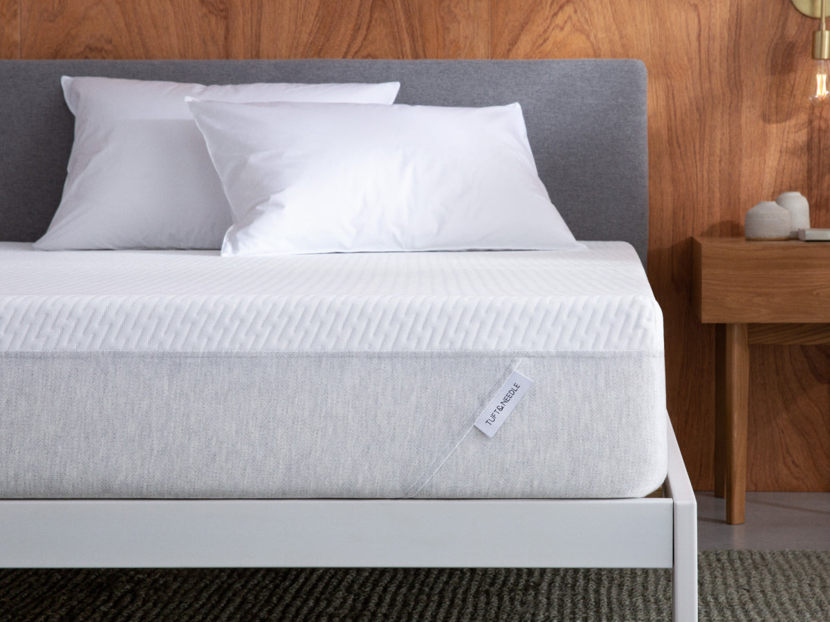 Tuft and needle mattress sitting in a white bedframe with 2 pillows on top