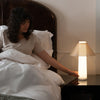 Woman sitting on a Tuft and Needle mattress leaning over and touching a Loftie Lamp on a night stand.