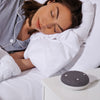 Woman asleep on her left side with a Snooz Go Travel White Noise Machine on her night stand